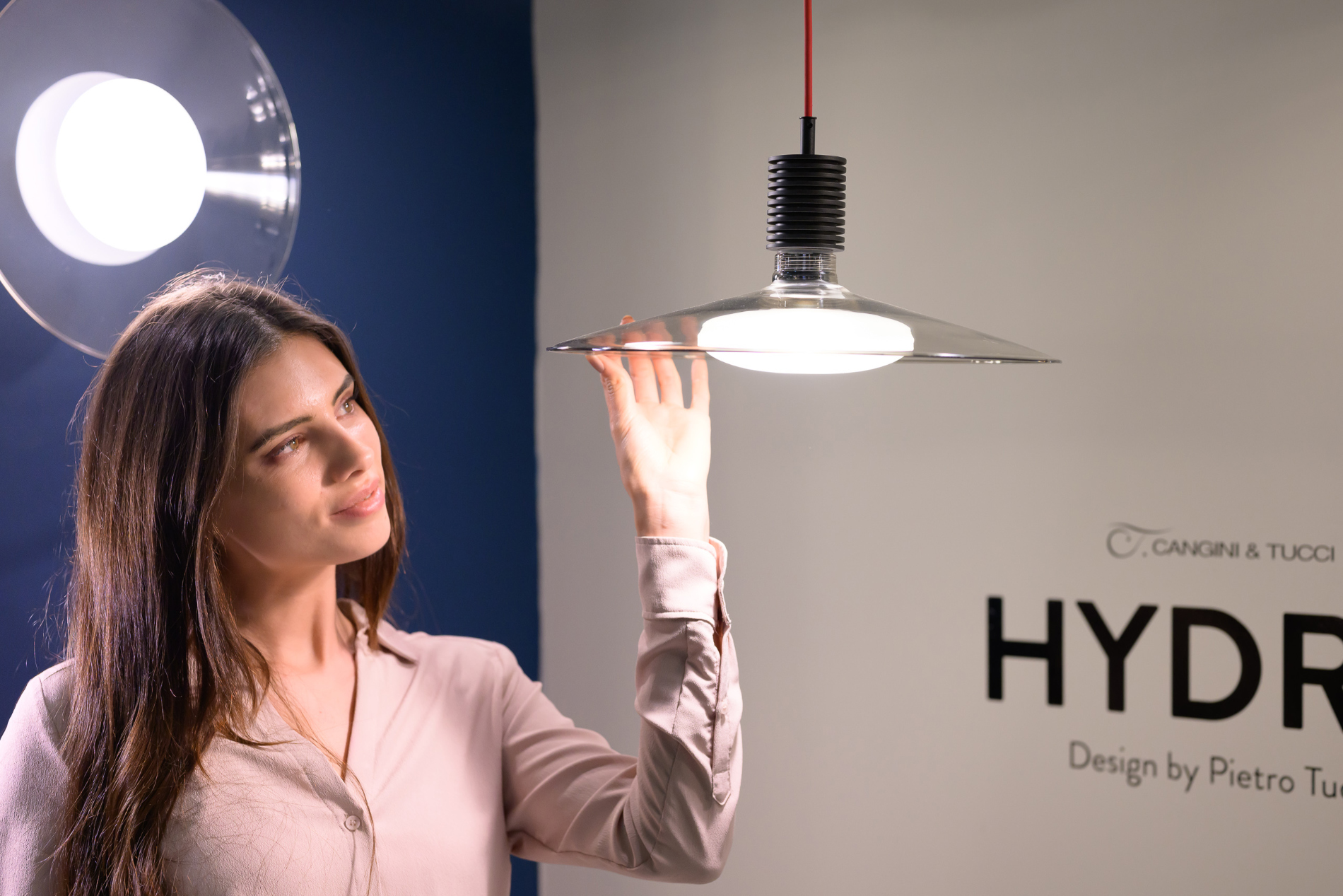 A woman stands in front of a hanging lamp.